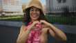 © Krakenimages.com - Woman wearing bikini and hat with a hawaiian lei making heart hands outdoors on a sunny street.