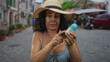 © Krakenimages.com - Woman wearing hat and bikini holds sunscreen on a sunny street, emphasizing skincare in an outdoor urban setting with blurred background
