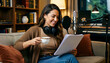 © Lubov - smiling woman records a podcast in her cozy home studio. She holds a white cup and script while sitting near a professional condenser microphone