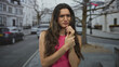 © Krakenimages.com - Young hispanic woman in a pink top holds her wrist with a pained frown on a busy street; injury recovery discomfort healing.