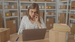 © Krakenimages.com - Woman holds phone to ear next to laptop and parcel box on table in building; productivity efficiency concentration.