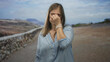 © Krakenimages.com - Young woman in light blue blouse pinches nose on street beside rocky embankment under sunlit sky; disgust.