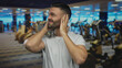 © Krakenimages.com - Young man in a gym covers his ears feeling overwhelmed by noise among exercise machines indoors under bright lights.