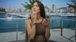 © Krakenimages.com - Woman holding smartphone with finger to lips on building terrace overlooking marina; contemplation calm.