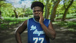 © Krakenimages.com - Man with hand on cheek for toothache in forest wearing blue basketball jersey and number 77, looking pained; toothache pain.