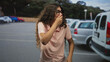 © Krakenimages.com - Woman wearing glasses covers mouth with hand while standing in a street parking lot beside parked cars and a van; surprise.