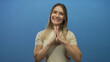 © Krakenimages.com - Woman smiling confidently with hands clasped in front against a solid blue background, embodying positivity and friendliness in an isolated setting.