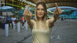 © Krakenimages.com - Woman making gesture in outdoor airport, young and blonde in casual attire with terminal in background, conveying defiance and attitude in a busy travel setting.