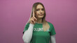 © Krakenimages.com - Woman volunteer with blonde hair gestures no on pink background in isolated setting, wearing green shirt with confident expression, emphasizing youth and communication.