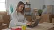 © Krakenimages.com - Young woman working on laptop in living room with moving boxes around in her new home indoors, smiling and relaxed.