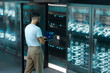 © Rendara Studio - Man analyzing network performance on laptop inside digital 3D data center