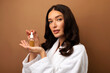 © Home-stock - Essential oils for skincare. Lady holding bottle with face serum, making beauty treatments, standing in bathrobe on brown background