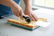 © Stitch - A person's hands using a rotary cutter and a clear ruler to precisely cut a stack of colorful fabrics for quilting.