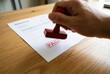 © Stitch - A hand is stamping an invoice with a red 'PAID' stamp on a wooden office desk, signifying a completed transaction.