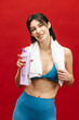 © wedmoments.stock - Sporty woman wrapped in towel holding a water bottle on red isolated background. Hydration, fitness recovery and healthy lifestyle concept.