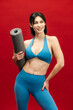 © wedmoments.stock - Sporty woman with yoga mat on red isolated background. Wellness, fitness and body care concept.