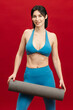 © wedmoments.stock - Sporty woman posing with a fitness mat on red isolated background. Fitness, wellness and active lifestyle concept.