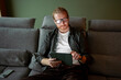 © Artcore Studio/Stocksy - Man using a tablet while sitting on a gray sofa in a living room
