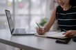 © Wasana - Woman writing notes while working on laptop