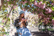 © svetograph - Cherryblossoms Spring Woman: Girl uses phone on park bench under blooming cherry trees during a sunny spring day.