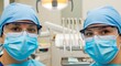 © MdNazim - Two women in blue medical scrubs and masks standing in a dental clinic with dental equipment