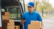 © MdNazim - Delivery man in blue uniform holding packages and checking smartphone near van blue cap