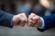 © Viral - Two businessmen in formal suits exchanging a fist bump outdoors, symbolizing partnership and teamwork