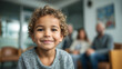 © AnastasiiaAkh - Smiling toddler with curly hair in modern clinic waiting room with family background