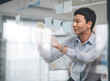 © dodotone - Business asian middle adult man using glass board adhesive note sticky ideas paper at indoors office