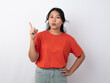 © Luqman Aditiamala - Attractive young Asian woman in orange shirt pointing to the copy space behind her, isolated by white background.