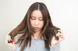 © KMPZZZ - Damaged Hair, frustrated asian young woman, girl hand in holding splitting ends, messy unbrushed dry hair with face upset, long disheveled hair, health care of beauty. Portrait isolated on background