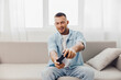 © SHOTPRIME STUDIO - Engaged man playing video games, showcasing excitement and joy in a cozy living room atmosphere filled with natural light. Perfect for gaming culture themes.