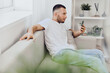 © SHOTPRIME STUDIO - Thoughtful man checking phone while sitting on a sofa, reflecting on his digital detox journey and work-life balance, amidst a calming home environment.