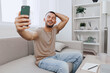© SHOTPRIME STUDIO - Happy man taking a selfie on a couch in a modern living room, showcasing the joy of casual moments and digital communication in 2025 style.