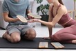 © New Africa - Young man and woman with sadhu boards on yoga mat at home, closeup