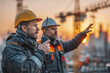 © Thanthara - Construction site communication concept two engineers in protective gear using walkie talkie discussing project progress at sunset with cranes in background