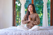 © Farknot Architect - Portrait image of a woman put hands together in a prayer and meditating on the bed at home