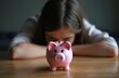 © Viktor - Young girl looks sadly at empty piggy bank. Child is upset, worried about savings, money issues, financial problems. Kid feels despair, loss of funds.
