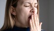 © waqi - A close-up shot of a fair-skinned woman yawning widely, covering her mouth with her hand. Her eyes are closed