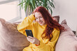 © Tatyana Gladskih - Smiling teenage girl sitting on couch and looking at phone screen