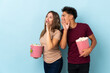 © luismolinero - Couple eating popcorn while watching a movie isolated on purple background shouting with mouth wide open to the lateral