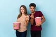 © luismolinero - Couple eating popcorn while watching a movie isolated on purple background inviting to come with hand. Happy that you came
