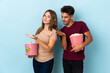 © luismolinero - Couple eating popcorn while watching a movie isolated on purple background extending hands to the side for inviting to come