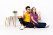 © luismolinero - Young couple sitting on the floor isolated on white background saluting with hand with happy expression