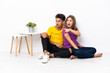 © luismolinero - Young couple sitting on the floor isolated on white background pointing to the side to present a product