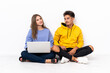 © luismolinero - Young couple with a laptop sitting on the floor isolated on white background posing with arms at hip and smiling