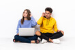 © luismolinero - Young couple with a laptop sitting on the floor isolated on white background having doubts