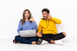 © luismolinero - Young couple with a laptop sitting on the floor isolated on white background making phone gesture. Call me back sign