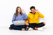 © luismolinero - Young couple with a laptop sitting on the floor isolated on white background listening to something by putting hand on the ear