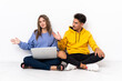 © luismolinero - Young couple with a laptop sitting on the floor isolated on white background extending hands to the side for inviting to come